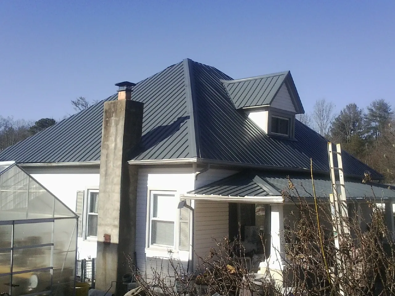Dark blue standing seam metal roof on a white farmhouse with dormer — Slate & Tile Roof Repair by Roofing Brothers in Hooppole