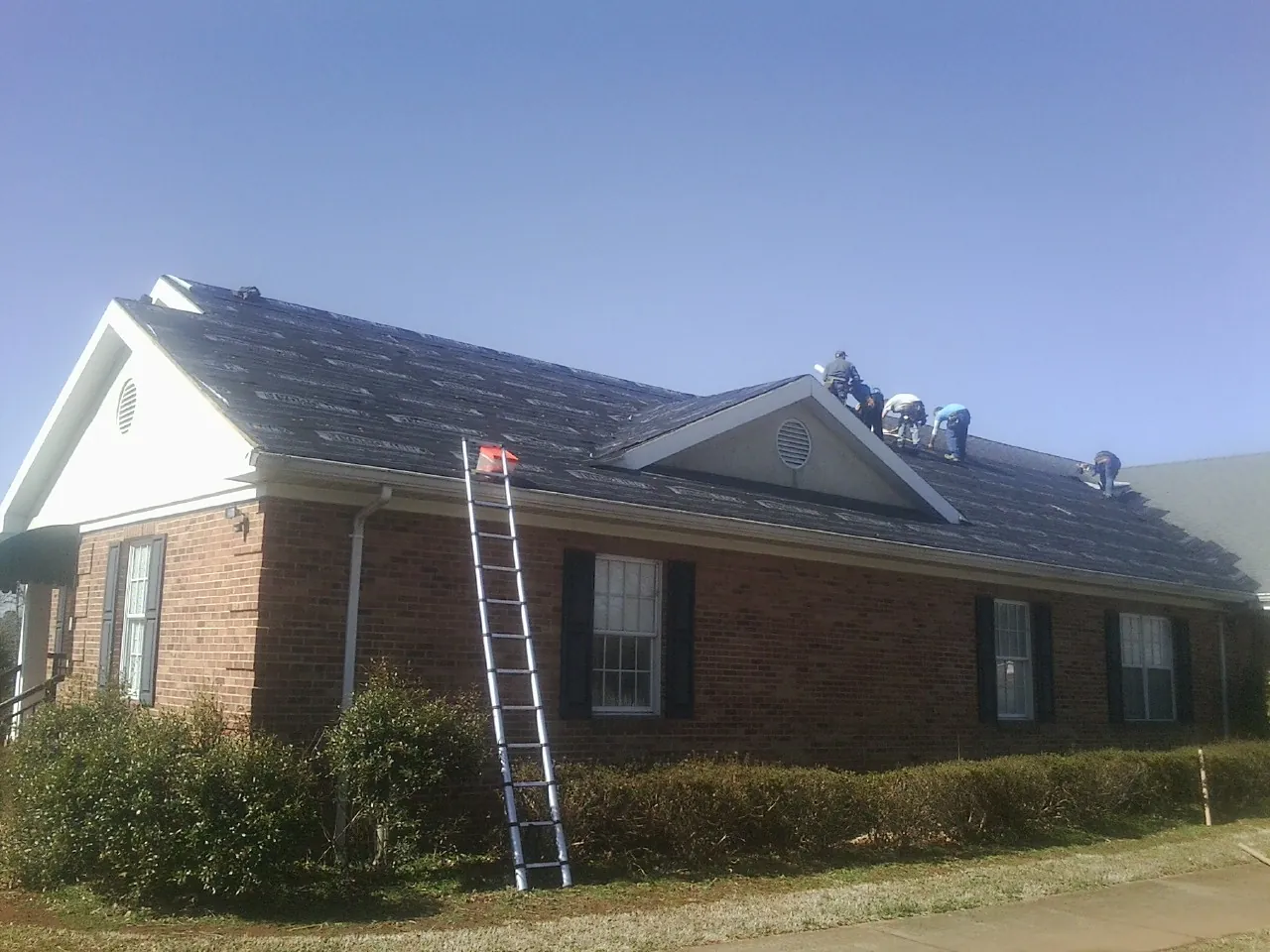 Crew tearing shingles off a brick ranch roof with a ladder set — Emergency Roof Repair work by our crew in Hooppole