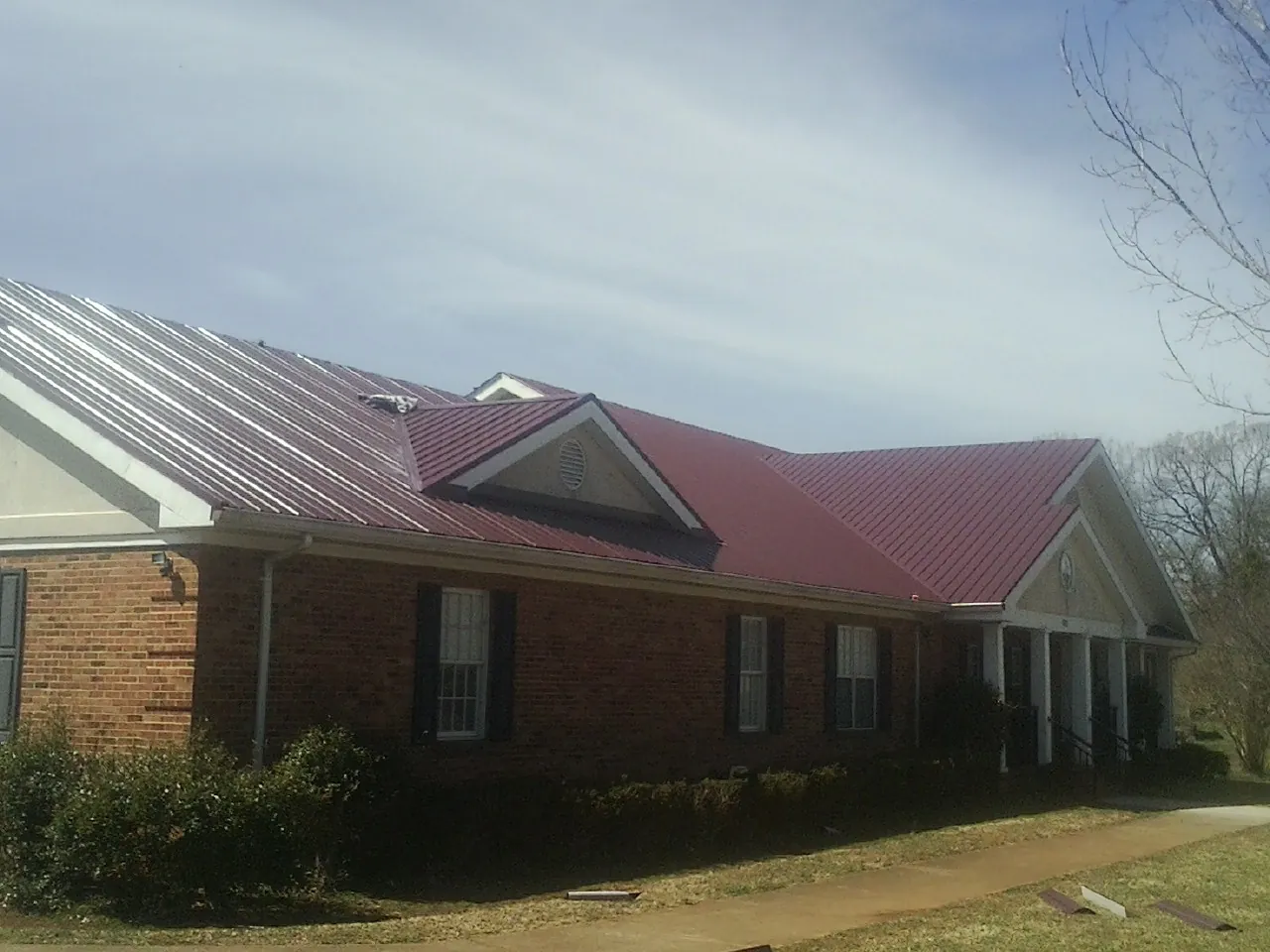 Red metal roof with gabled entries on a long brick building, from a Hail Damage Roof Repair job in Hooppole