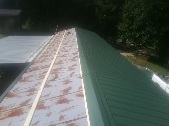 Old rusted panels beside newly installed green metal roofing — Wind Damage Roof Repair by Roofing Brothers in Hooppole