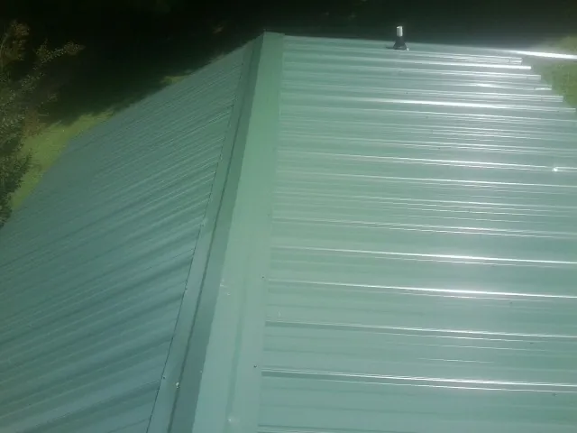 New green metal panels meeting at the ridge of a roof — Flat Roof Repair work by our crew in Hooppole