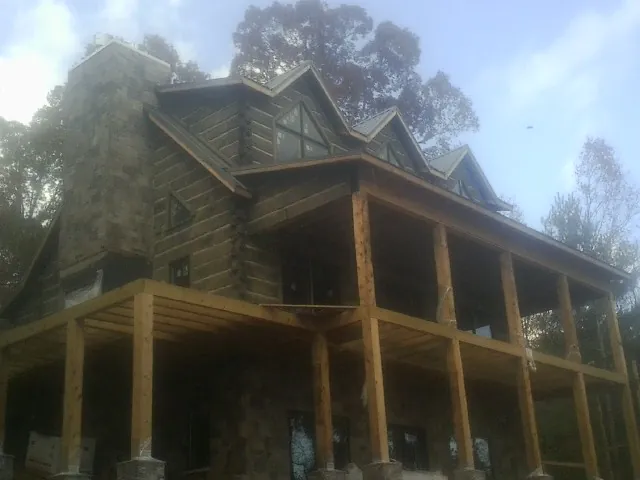 Stone chimney and dormers on a large log home with a timber porch in Hooppole