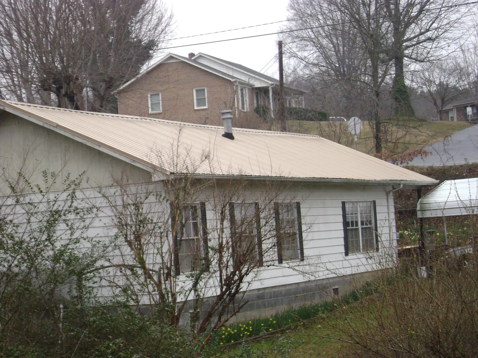 Tan metal roof on a white sided house set into a hillside — Commercial Roofing by Roofing Brothers in Hooppole