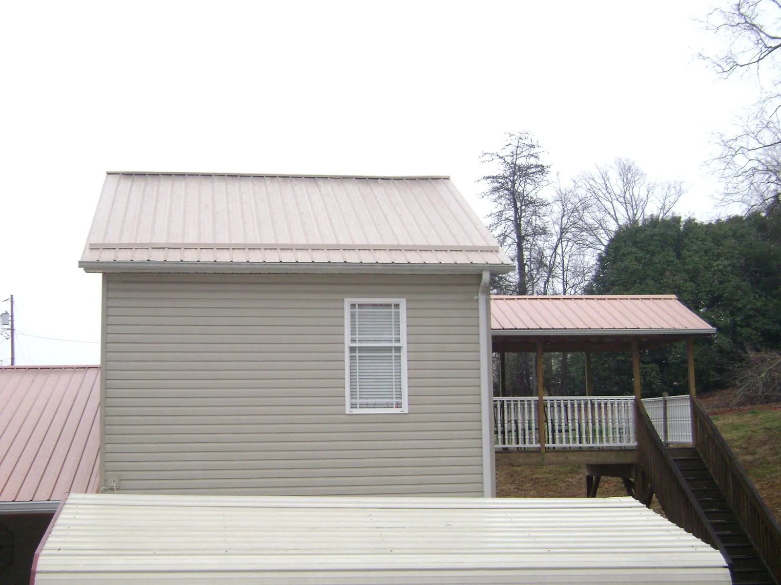 Tan metal roofs on a two story addition and attached porch, from a Roof Replacement job in Hooppole